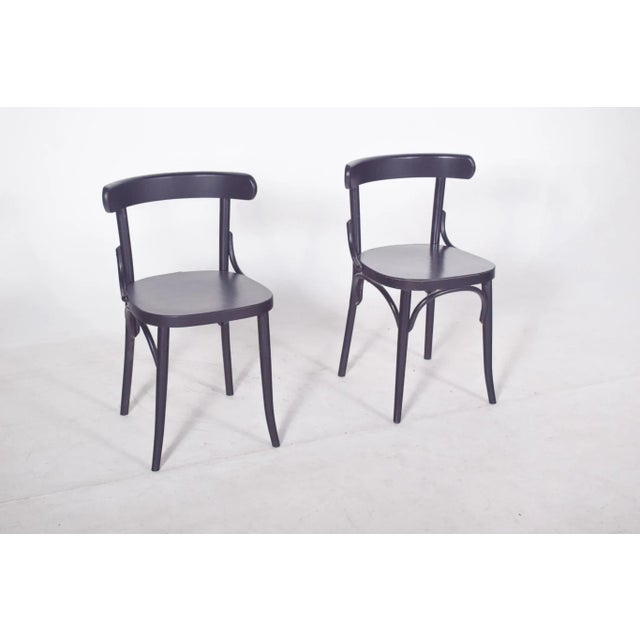 Pair of black painted chairs with a low, curved backrest that extends laterally in a continuous, smooth line,...