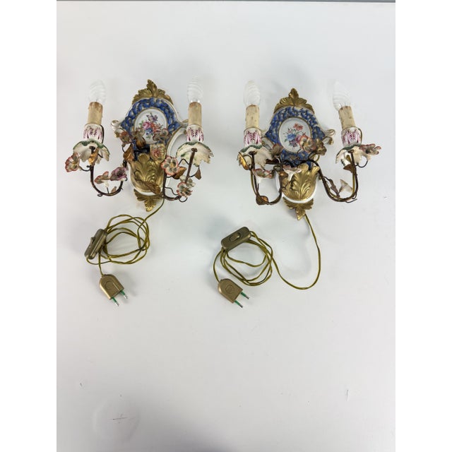 Set of two 2-light wall lamps in wrought iron and decorated porcelain, 1940s Intact and in good condition. Minor signs of...