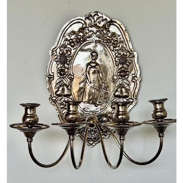 An elegant pair of antique European wall sconces, each featuring a richly worked silvered metal backplate centered with a...