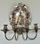 An elegant pair of antique European wall sconces, each featuring a richly worked silvered metal backplate centered with a...