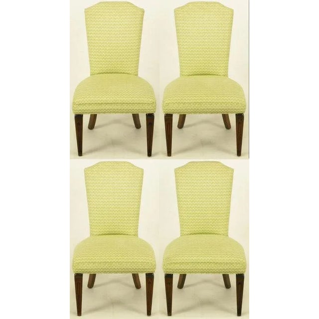 Set of four regency side chairs with carved and tapered walnut front legs and saber back legs. Upholstery is an apple...