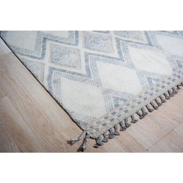This hand knotted pile rug features a distinct Berber carpet style made from high-quality wool. The primary color palette...