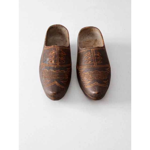 This is a pair of antique wooden clogs, hand-carved with decorative patterns across the feet. The warm patina and...