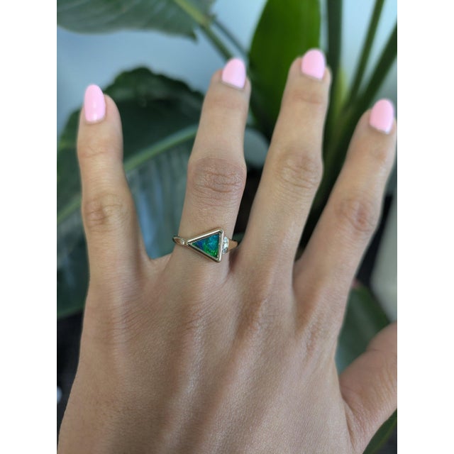 A solid natural boulder opal glows with green and blue fire in a trillion cabochon at the centre of this solid 14K yellow...