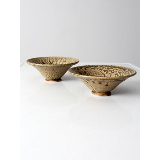 A pair of vintage handmade studio pottery bowls featuring a richly layered glaze in warm tan tones with dark brown and...