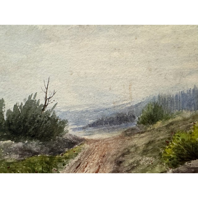 Original watercolor on textured paper depicting a winding country road through rocky green terrain toward distant blue-...