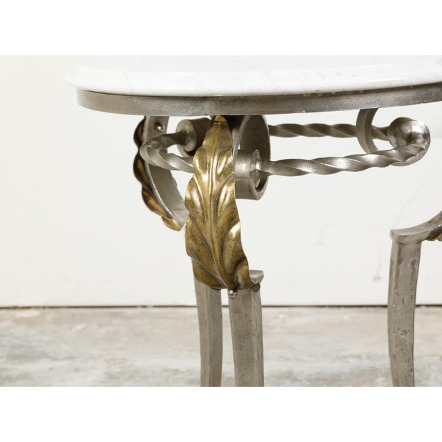 An Italian steel side table from the mid 20th century, with white veined marble top, acanthus leaves and hoofed feet....