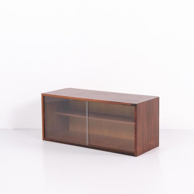 Wall-mounted cabinet crafted from rosewood with glass doors. The cabinet was made in the 1960s and represents Danish...