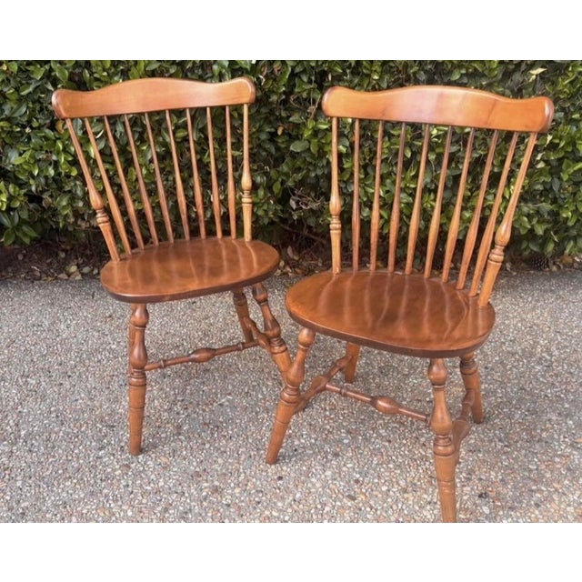 A handsome pair of vintage Windsor-style spindle-back side chairs crafted in warm-toned wood with shaped crest rails,...