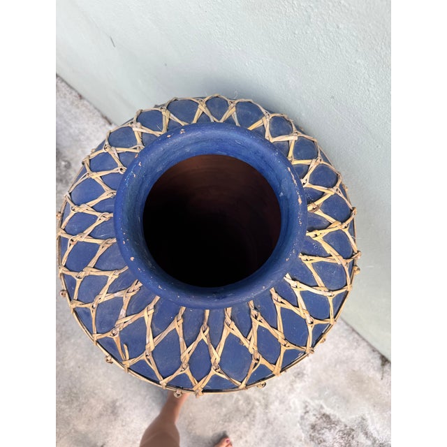 A substantial blue-glazed terracotta vessel enveloped in a hand-tied rattan lattice exterior that softens and grounds the...