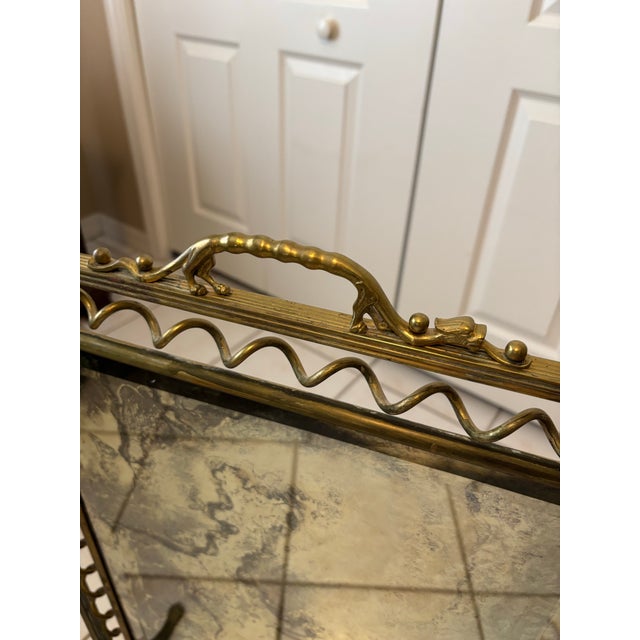 A distinctive vintage brass freestanding mirror designed as a decorative fireside or floor accent. This sculptural piece...