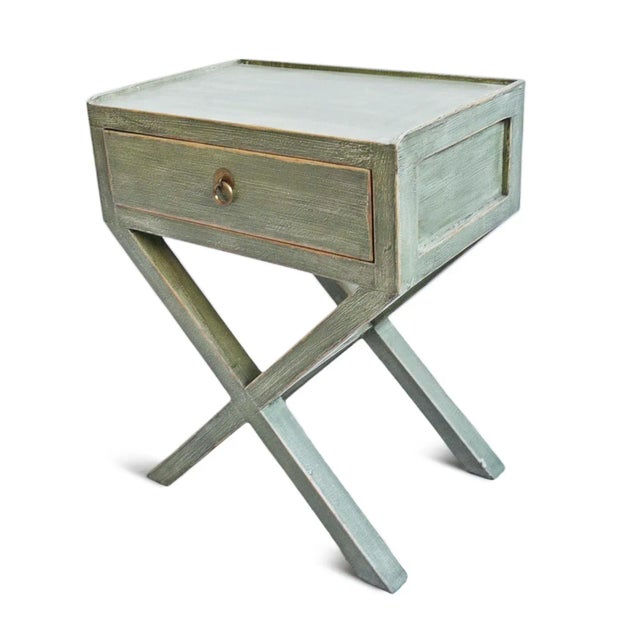 Farmhouse vintage style green washed finish wood bedside table with X design base. One drawer for storage with brass...