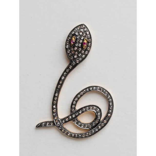 A pair of coiled snake earrings with round, brilliant cut diamonds set in rhodium plating with faceted ruby eyes. 18K gold...