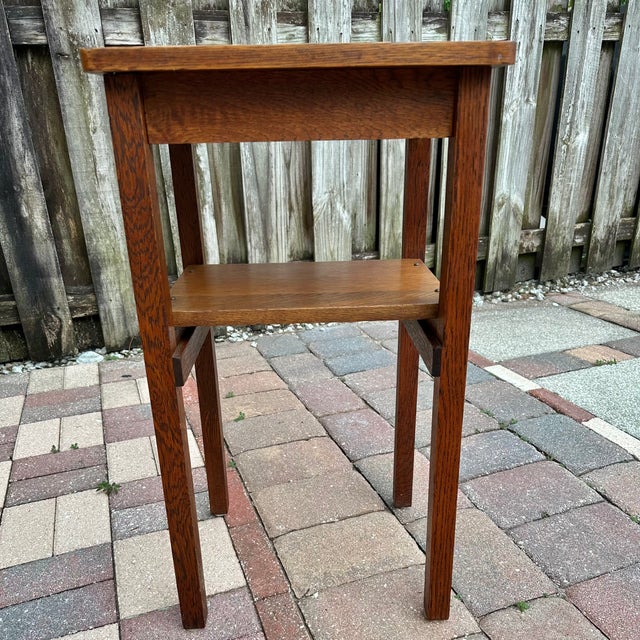 Solid wood plant stand or small side table with a simple, functional Arts & Crafts–style design. The piece features a...