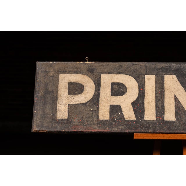 Long, narrow wooden trade sign with bold, hand-rendered "PRINTING" lettering across a black-painted ground. The surface...