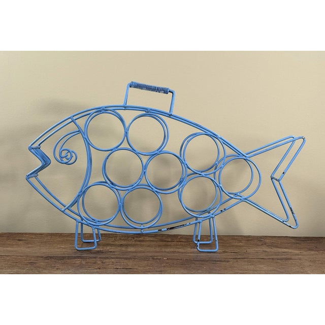 This mid century modern wire wine bottle holder is formed as a stylized fish in bright blue painted metal with circular...