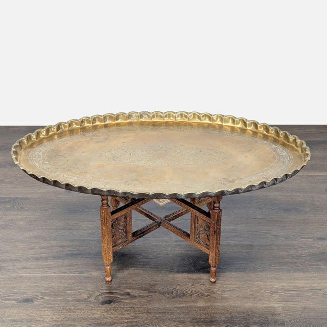 Brass etched tray table, hand tooled in exquisite foliate designs, with a hammer folded pie-crust edge. The tabletop rests...