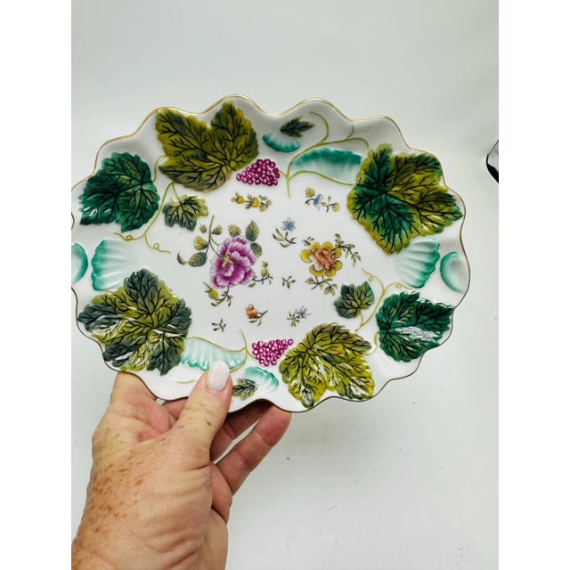 This is a decorative porcelain serving dish with a scalloped edge. It features a floral and leaf motif in vibrant green,...