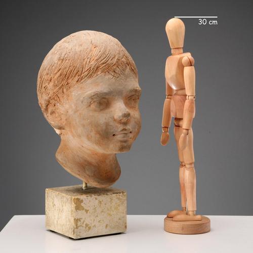 Terracotta sculpture on a travertine marble base depicting the portrait of a young boy. Engraved signature of the artist....