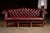 Hand-tufted oxblood leather camelback sofa with rolled arms, brass nailhead trim, and a solid mahogany base frame. The...
