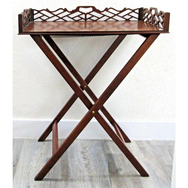 The 1920s Antique Pierced Mahogany Baker Furniture Folding Butler Tray and Stand is a vintage tray top table set made of...