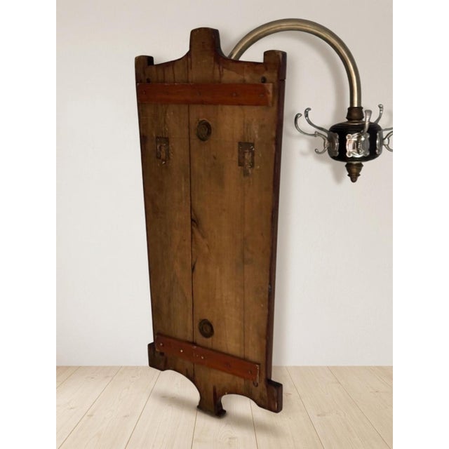 A distinctive vintage wooden coat rack featuring a decorative wooden back panel, multiple curved metal hooks, and a...