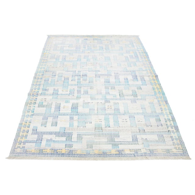 This rug showcases a contemporary Kilim flatweave pattern crafted from wool. It features a beige base with an abstract...