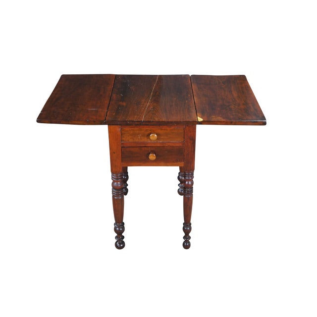 Antique cherry drop leaf side accent table. This table features American federal styling with dropleaf sides, two drawers,...