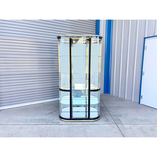 This striking vintage Hollywood Regency display cabinet features a sleek oval silhouette styled after iconic Mastercraft...
