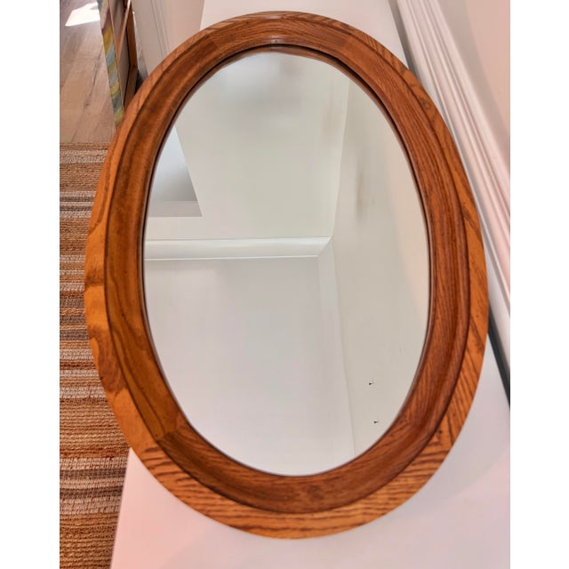 Handsome vintage oval wall mirror featuring a substantial oak wood frame with a warm walnut-stained finish, beautifully...