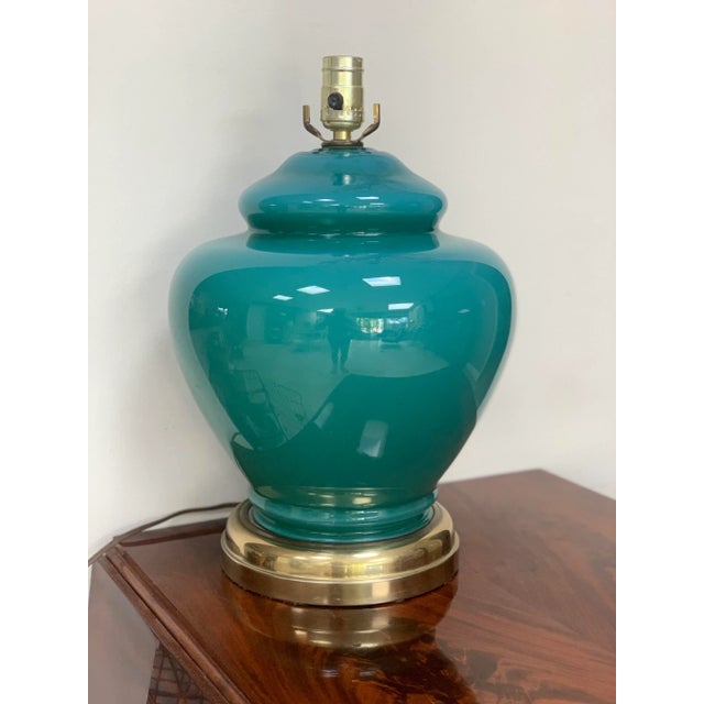 Vintage, glass encased table lamp in a deep teal color set on a brass plinth. The large ginger jar shape on the brass...