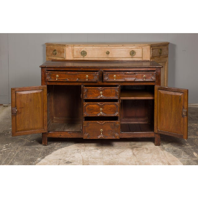 An English oak dresser base from the 19th century with geometric front, five drawers, two doors and brass hardware....