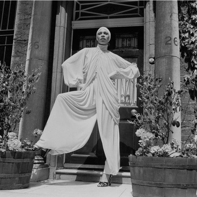 Fashion, 1975 A female fashion model wearing a drapped high collar neck top with matching extra wide leg trousers and hat,...