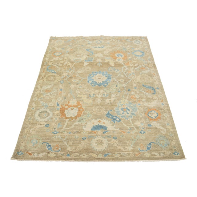 This hand-knotted wool rug features a light brown background with multicolored all-over designs. This rug measures 6'1'' x...