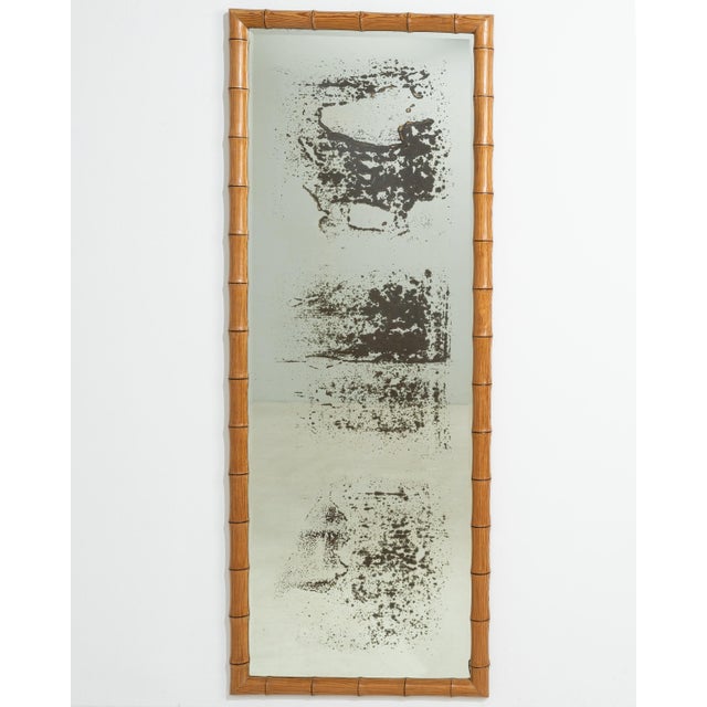 A 20th century French wall mirror designed in the faux bamboo style, crafted in carved wood. The frame imitates natural...