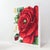 This striking vintage needlework piece features a vibrant, large-scale red rose blossom as its central focus, rendered in...