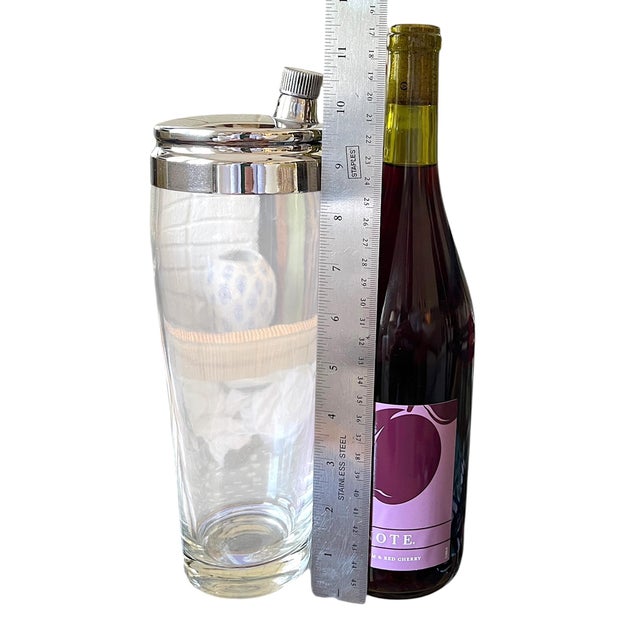 A striking mid-century cocktail shaker featuring a substantial glass body paired with a polished chrome lid and integrated...