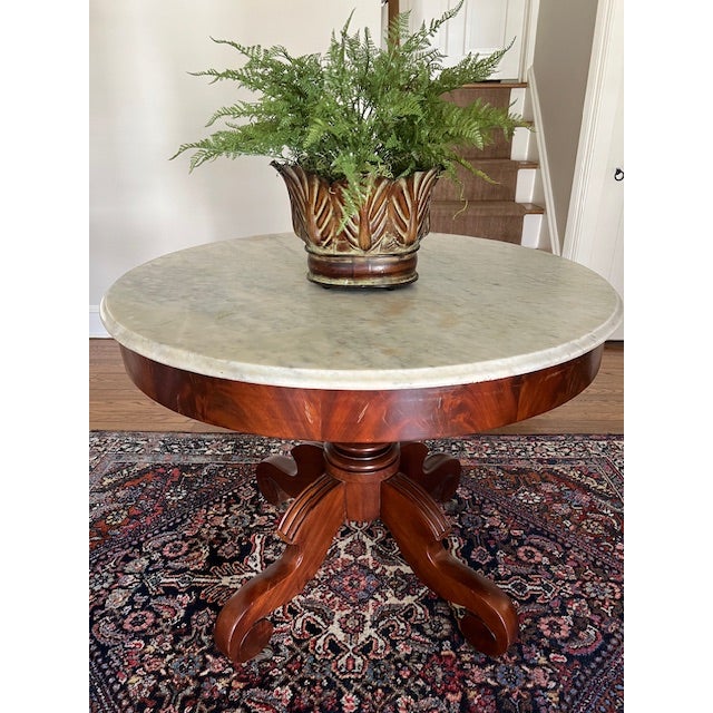 An elegant antique mahogany center table with marble top is offered for sale. The mahogany base has lovely lines and...