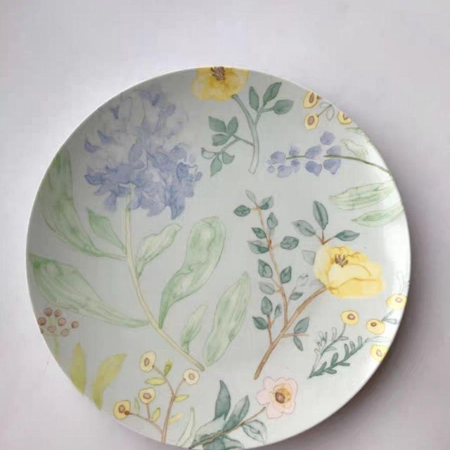 This vintage-inspired ceramic plate features hand-painted watercolor floral motifs in soft pastels—including pale blue...