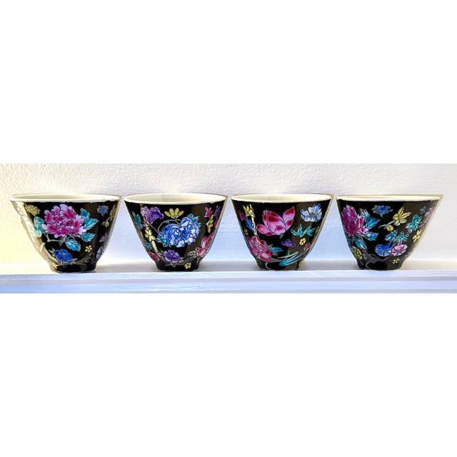 Four Chinese porcelain teacups in the Famille Noire pattern made in China. The background is black with a beautiful floral...