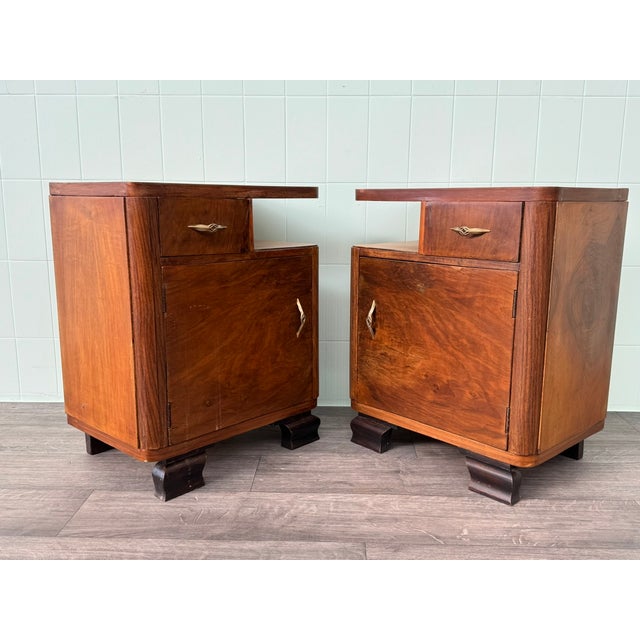 Pair of 1930s bedside tables featuring a top drawer, an open side compartment, a main door, and solid, molded, and shaped...