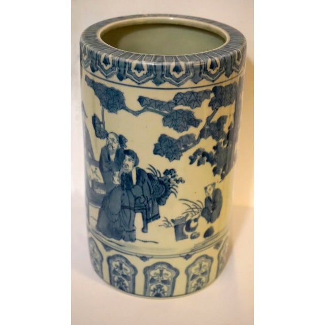 This porcelain blue and white bough pot vase depicts scenes with scholars possibly at an outdoor desk. It is cylindrical...