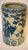 This porcelain blue and white bough pot vase depicts scenes with scholars possibly at an outdoor desk. It is cylindrical...