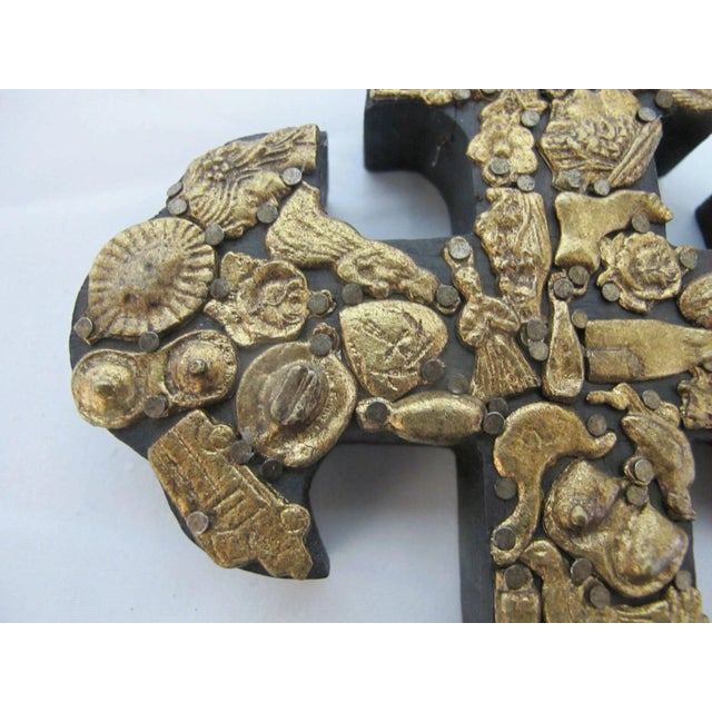 Traditional Mexican folk art Milagros cross featuring a hand-carved dark wood base densely embellished with hammered gold-...