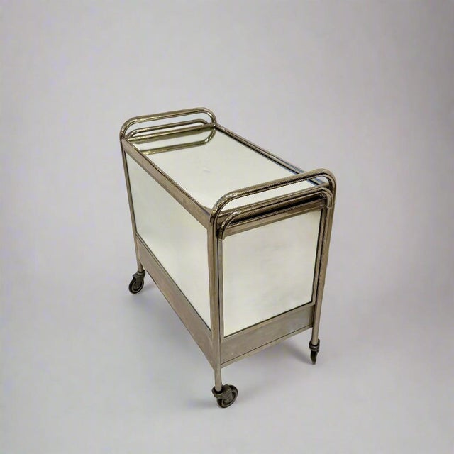 An Art Deco bar cart, made of polished nickel frame with mirrored surfaces and pull out extension trays on either side....