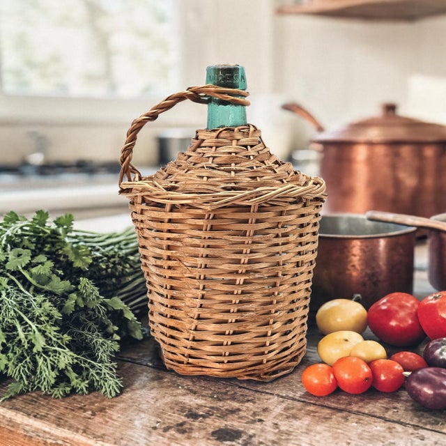 A vintage green glass demijohn bottle encased in a hand-woven wicker basket, embossed with the name “Viressa.” This...