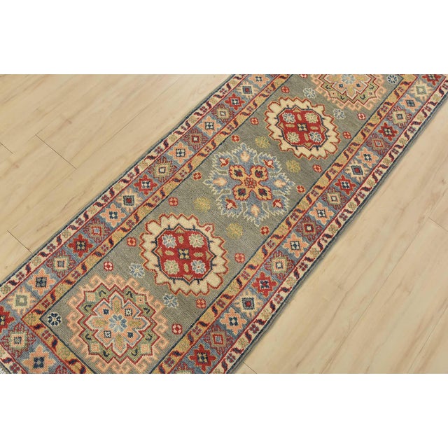 A tribal Caucasian Kazak runner hand-knotted with fine wool on a cotton foundation. This rug features a row of geometric...