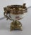 A small porcelain bowl with a fine polychrome flower design on a cream background. It is mounted on bronze, with a wide...