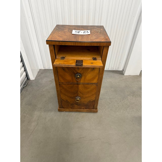This is an antique Biedermeier commode. It has a pull down lid, a cabinet, and a drawer. The wood is burled walnut. The...