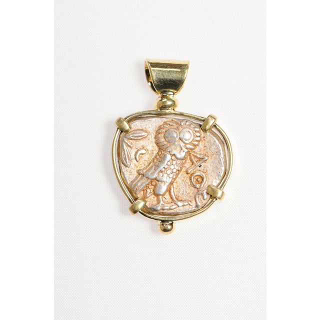 An Owl and Athena coin pendant set in 18kt gold from 454-404 BC, Athens. A silver tetradrachm coin with an owl and AOE on...